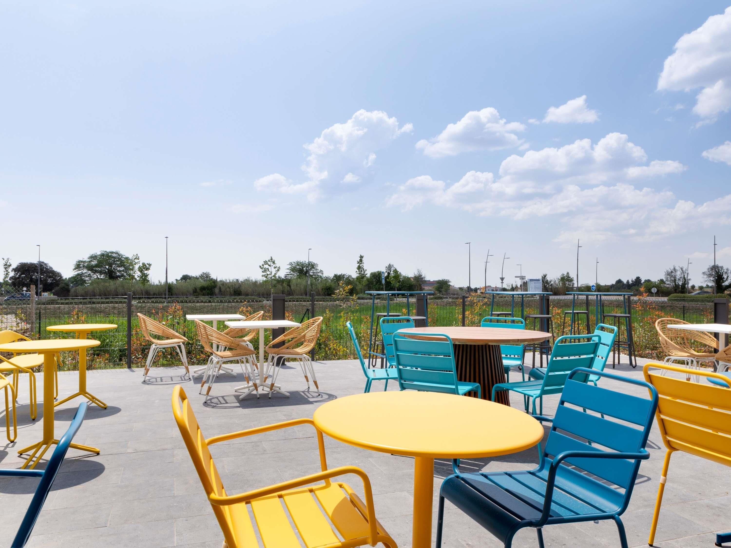 An outdoor seating area with round tables and chairs, a clear sky, and a view of the surrounding landscape.