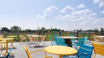 An outdoor seating area with round tables and chairs, a clear sky, and a view of the surrounding landscape.