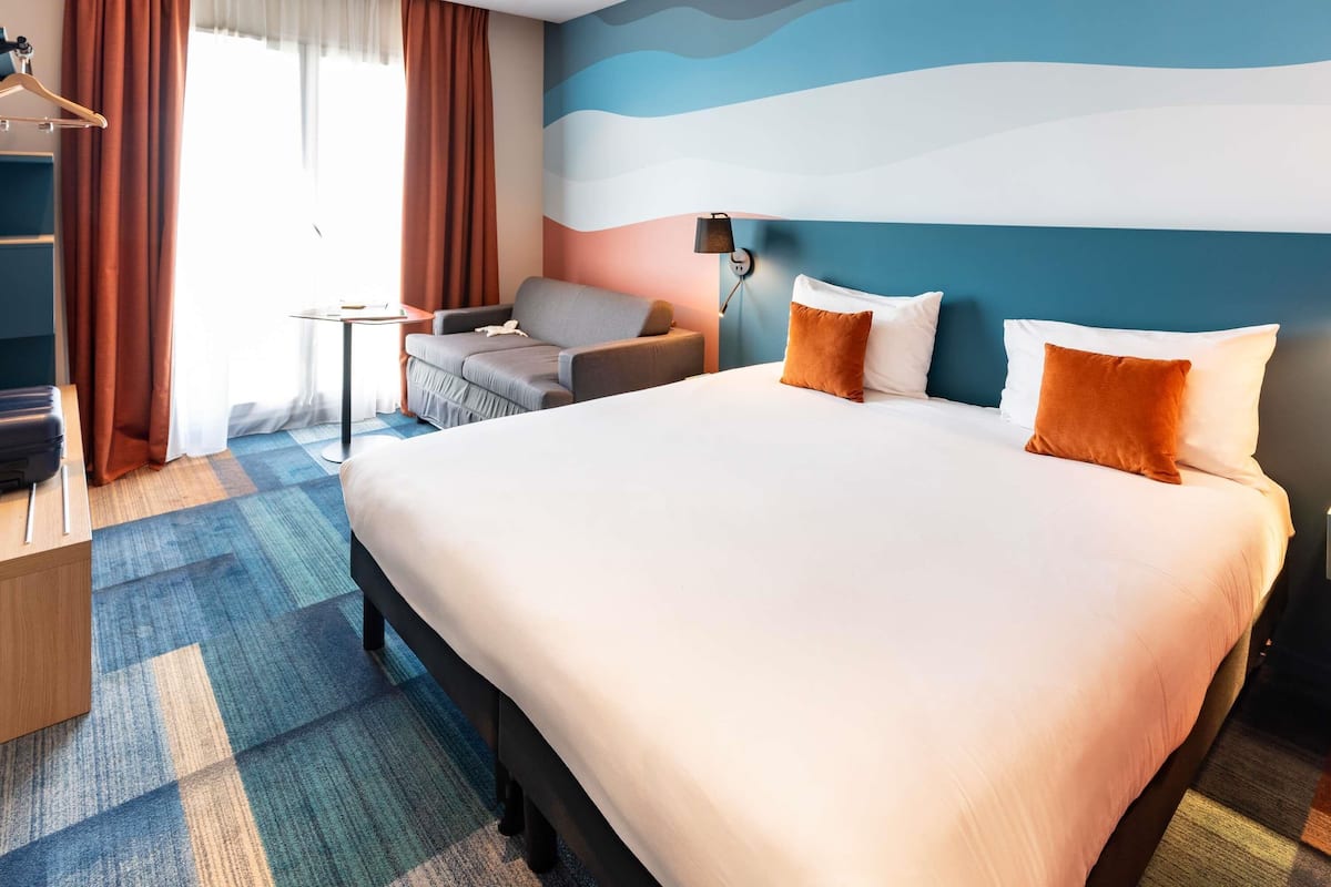 Quarto de hotel com cama grande, sofá, mesa pequena e guarda-roupa.