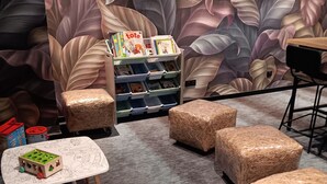 A cozy children's play area with a bookshelf, a table, and cushioned seating. - Ibis Styles Miramas - Provence (Miramas)
