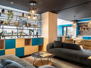 A modern interior with a blue and beige color scheme, featuring a sofa, a round table, and a bookshelf with plants. - Ibis Styles Miramas - Provence (Miramas)