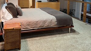 Une chambre à coucher avec un lit, une table de chevet, une lampe et une vue sur l’extérieur.