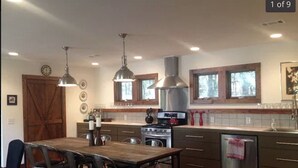 Une cuisine moderne dotée d’un îlot central, d’appareils électroménagers en acier inoxydable, de luminaires suspendus et d’une grande table à manger en bois.