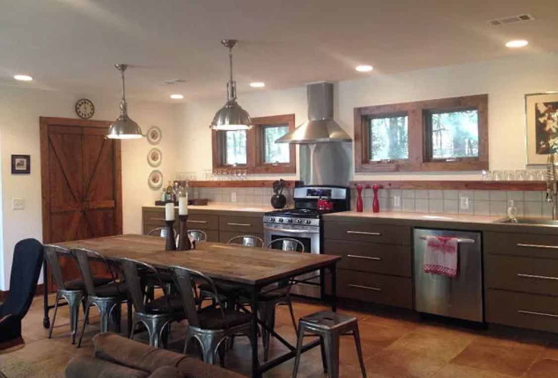 A modern kitchen with a central island, stainless steel appliances, pendant lighting, and a large wooden dining table.