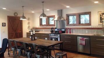 A modern kitchen with a central island, stainless steel appliances, pendant lighting, and a large wooden dining table.