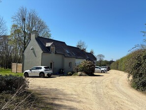 A two-story house with a sloped roof, a gravel driveway, and parked cars.
