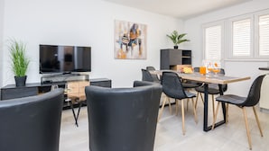 A modern living room with a flat-screen TV, a dining area with a wooden table and black chairs, a potted plant, and a painting on the wall. - Apartments Loncar (Vir)