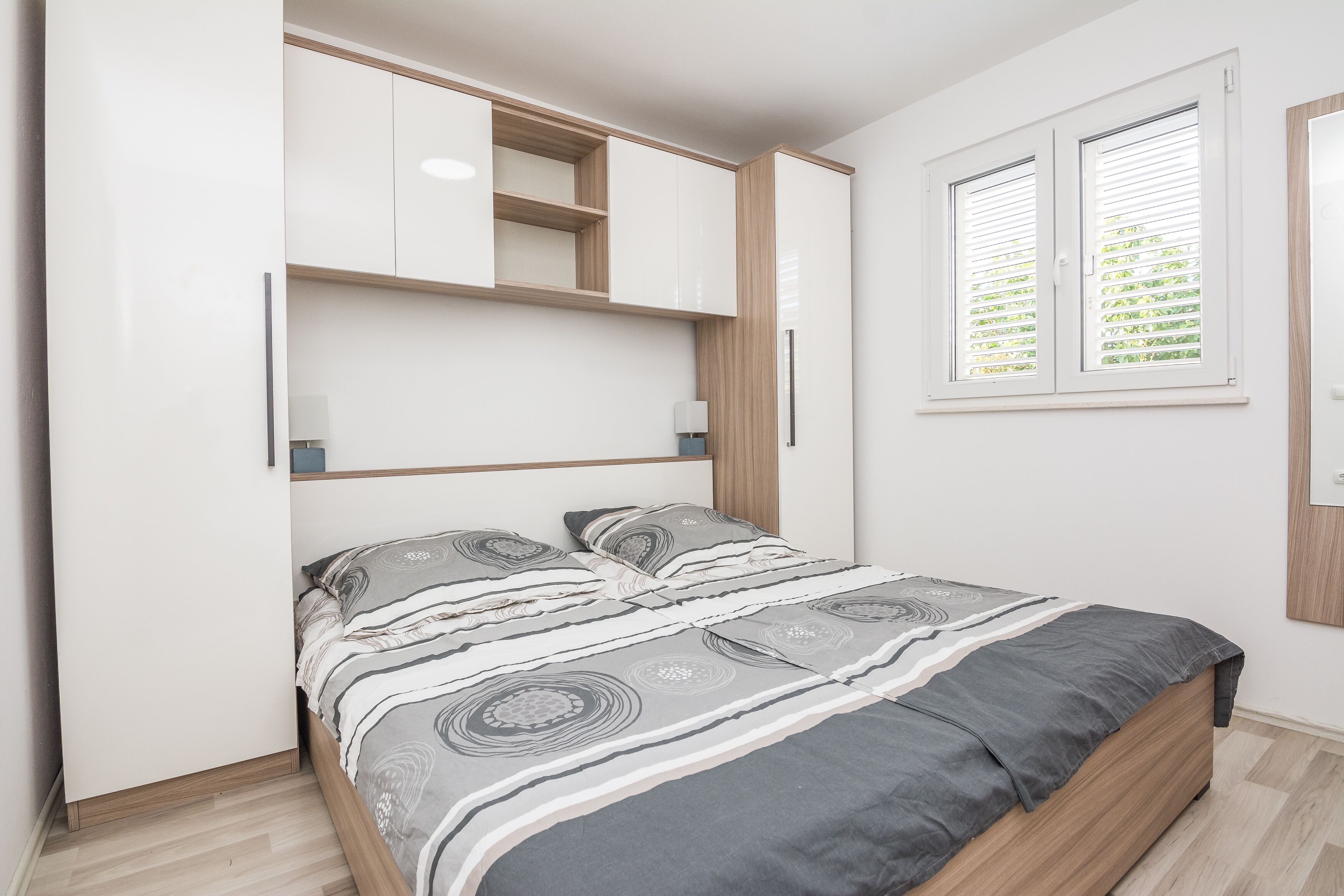 A bedroom with a bed, built-in shelving, and a window with blinds.