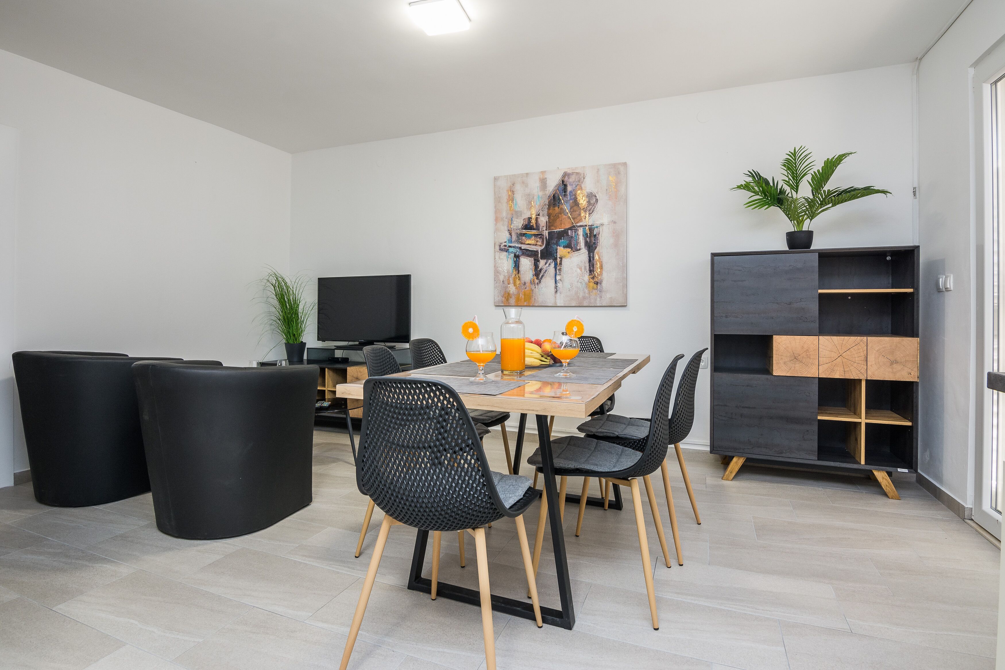 Een moderne eetruimte met een houten tafel, zwarte stoelen en een zwarte kast met een plant.