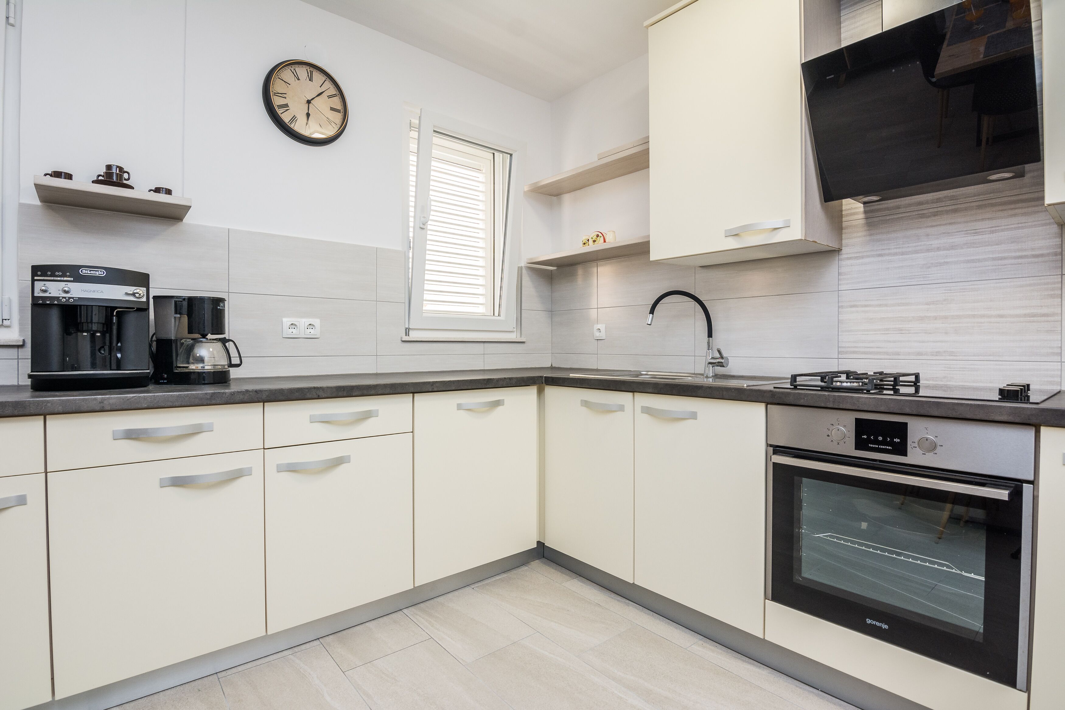 A modern kitchen with white cabinets, a coffee maker, a stove, and a built-in oven.