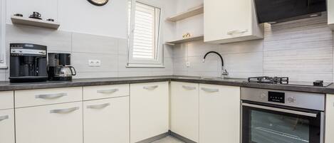 A modern kitchen with white cabinets, a coffee maker, a stove, and a built-in oven.
