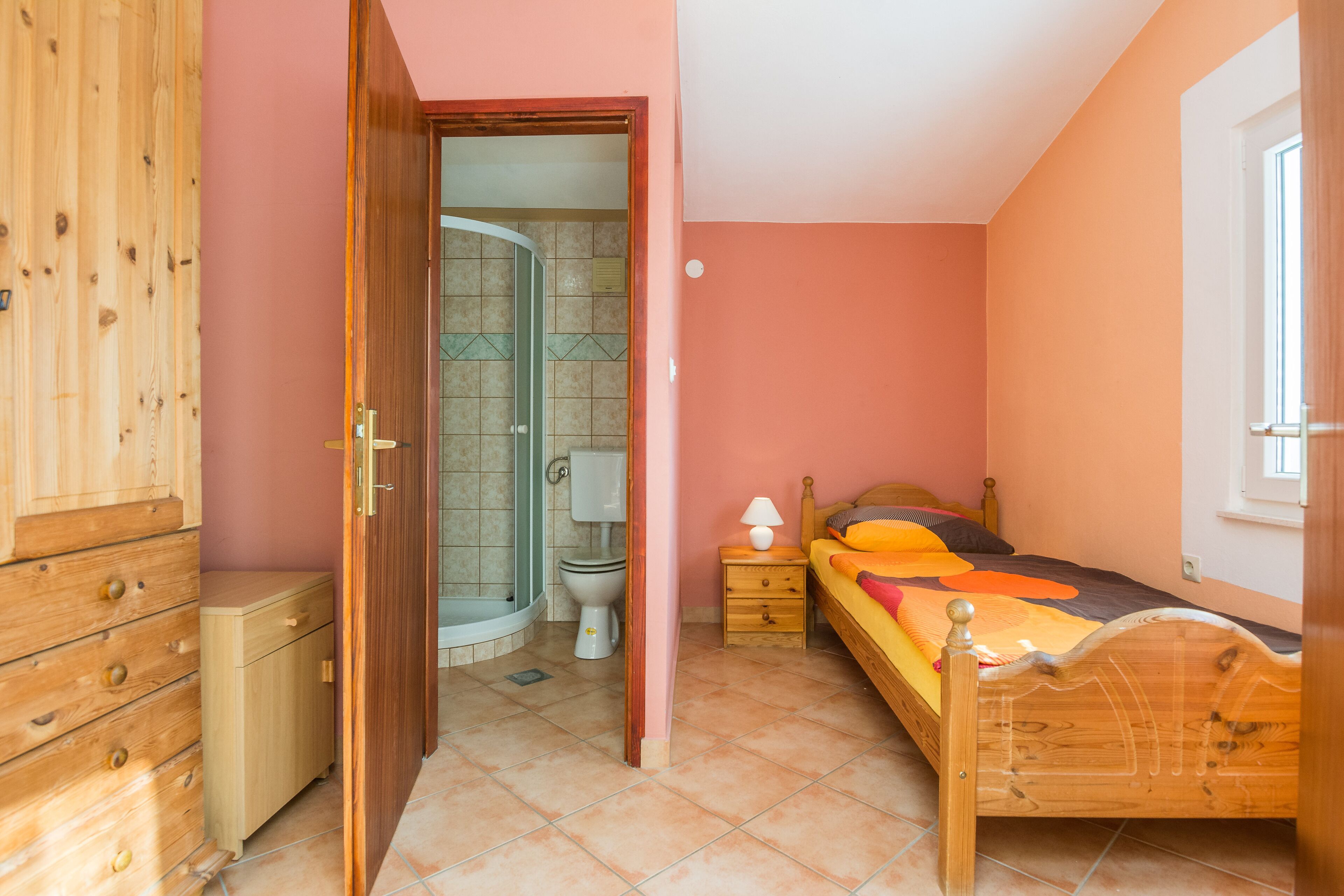Ein Schlafzimmer mit einem hölzernen Bett, einem Nachttisch, einem Holzschrank und einem Badezimmer mit Dusche und Toilette.