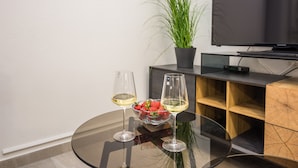 A modern living room with a glass table, two wine glasses, a bowl of strawberries, and a potted plant. - Apartments Loncar (Vir)