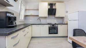 A modern kitchen with light-colored cabinets, a built-in oven, a coffee machine, and a refrigerator. - Apartments Loncar (Vir)