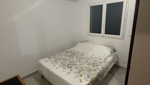 Een kleine kamer met een enkel bed, een raam, een nachtkastje en een deur.