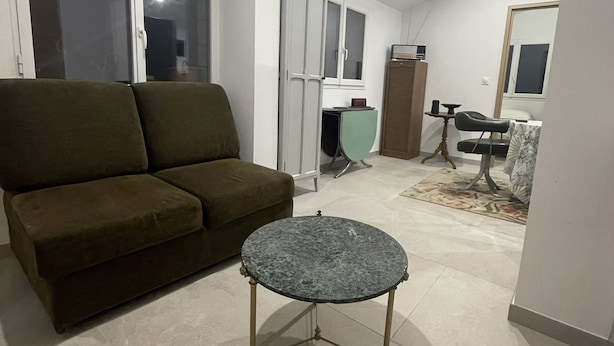 Een woonkamer met een groene bank, een ronde tafel en een kast.