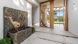 A modern entrance with a marble wall, a stone planter, and a view of a pool and mountains. - RDR234 - Amazing modern villa located minutes from beach (Marbella)
