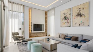 A modern living room with a sofa, ottomans, a coffee table, and a TV mounted on a stone wall. - RDR234 - Amazing modern villa located minutes from beach (Marbella)
