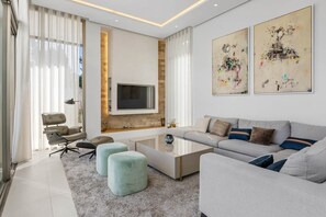 Una sala de estar moderna con un sofá, otomanas, una mesa de centro y un televisor montado en una pared de piedra.