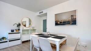 A modern dining area with a white table, four chairs, a round mirror, and a cityscape painting. - RDR274 - NEW 3 bedroom Apt with pool + near beach (Estepona)