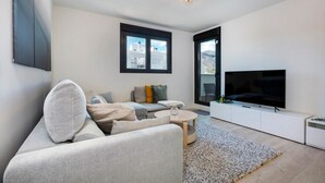 A modern living room with a sofa, coffee table, TV, and large windows. - RDR274 - NEW 3 bedroom Apt with pool + near beach (Estepona)