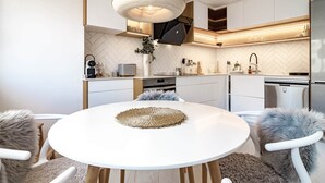 Une cuisine moderne avec des meubles blancs, une table de salle à manger ronde surmontée d’un set de table en fibres tressées et des chaises moelleuses.