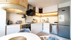 Une cuisine moderne avec des meubles blancs, un réfrigérateur en acier inoxydable et un luminaire suspendu.