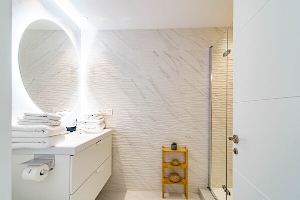 A bathroom with a marble wall, a wooden shelf with a plant, and a glass shower enclosure.