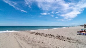 Une plage avec un ciel dégagé, un rivage sablonneux et quelques personnes qui prennent un bain de soleil.