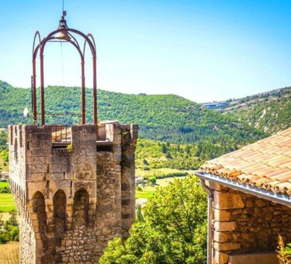 Una torre de piedra con ventanas de arco y una estructura metálica en la parte superior, frente a colinas verdes y un cielo despejado.