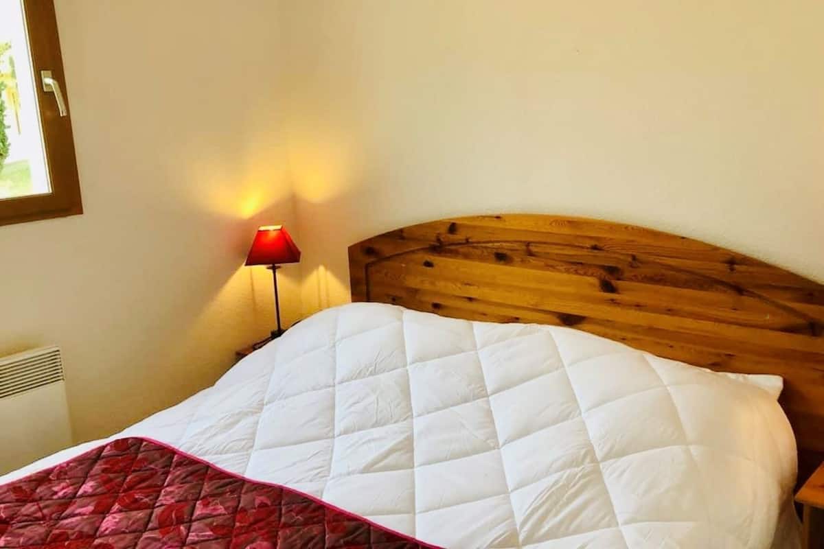 Una cama bien hecha con cabecera de madera, dos lámparas de noche y una colcha acolchada roja y blanca.