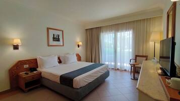 A hotel room with a bed, bedside tables, a desk with a chair, a television, and a window with curtains.