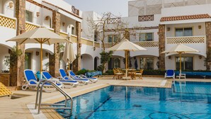 A pool area with lounge chairs and umbrellas, surrounded by a building with stone pillars and balconies. - Camel Dive Club & Boutique Hotel (Sharm El Sheikh)