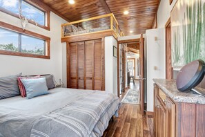 A bedroom with a loft bed, wooden ceiling, and a large window.