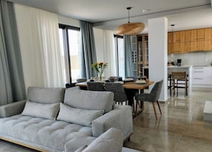 Ein modernes Wohnzimmer mit grauem Sofa, Essbereich mit Holztisch und -stühlen sowie eine Küche mit Holzschränken.