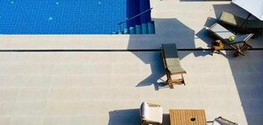 Ein Poolbereich auf dem Dach mit Liegestühlen und einem Tisch, mit Blick auf einen Swimmingpool.