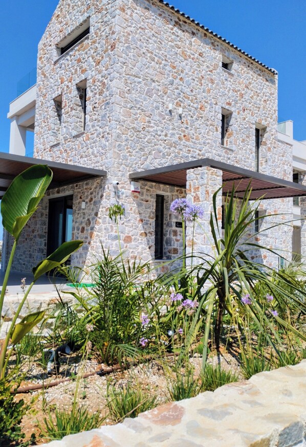 Un edificio de piedra de diseño moderno, con un balcón y un jardín con plantas y flores.