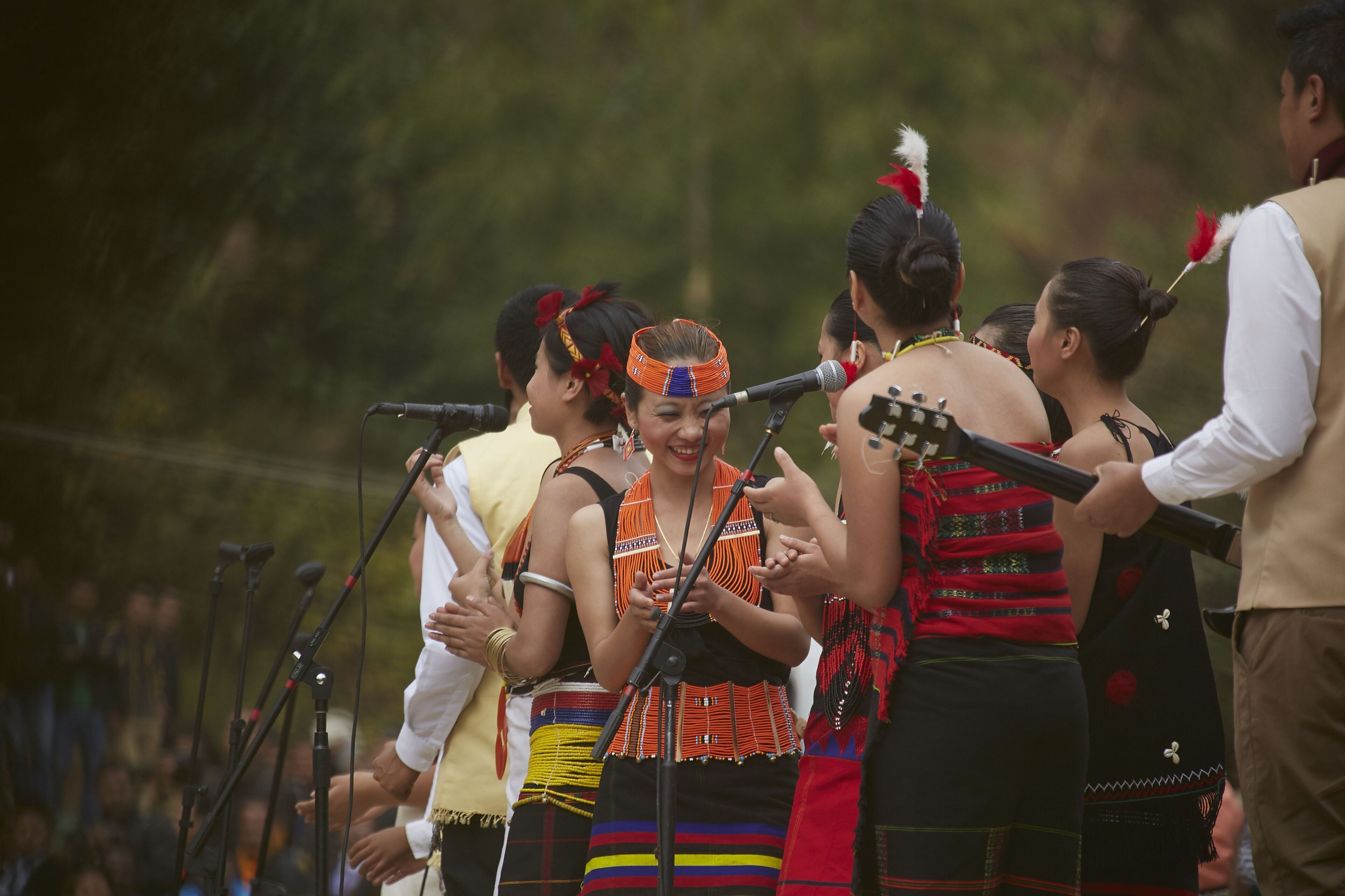 A group of people in traditional attire performing on stage with microphones and musical instruments.