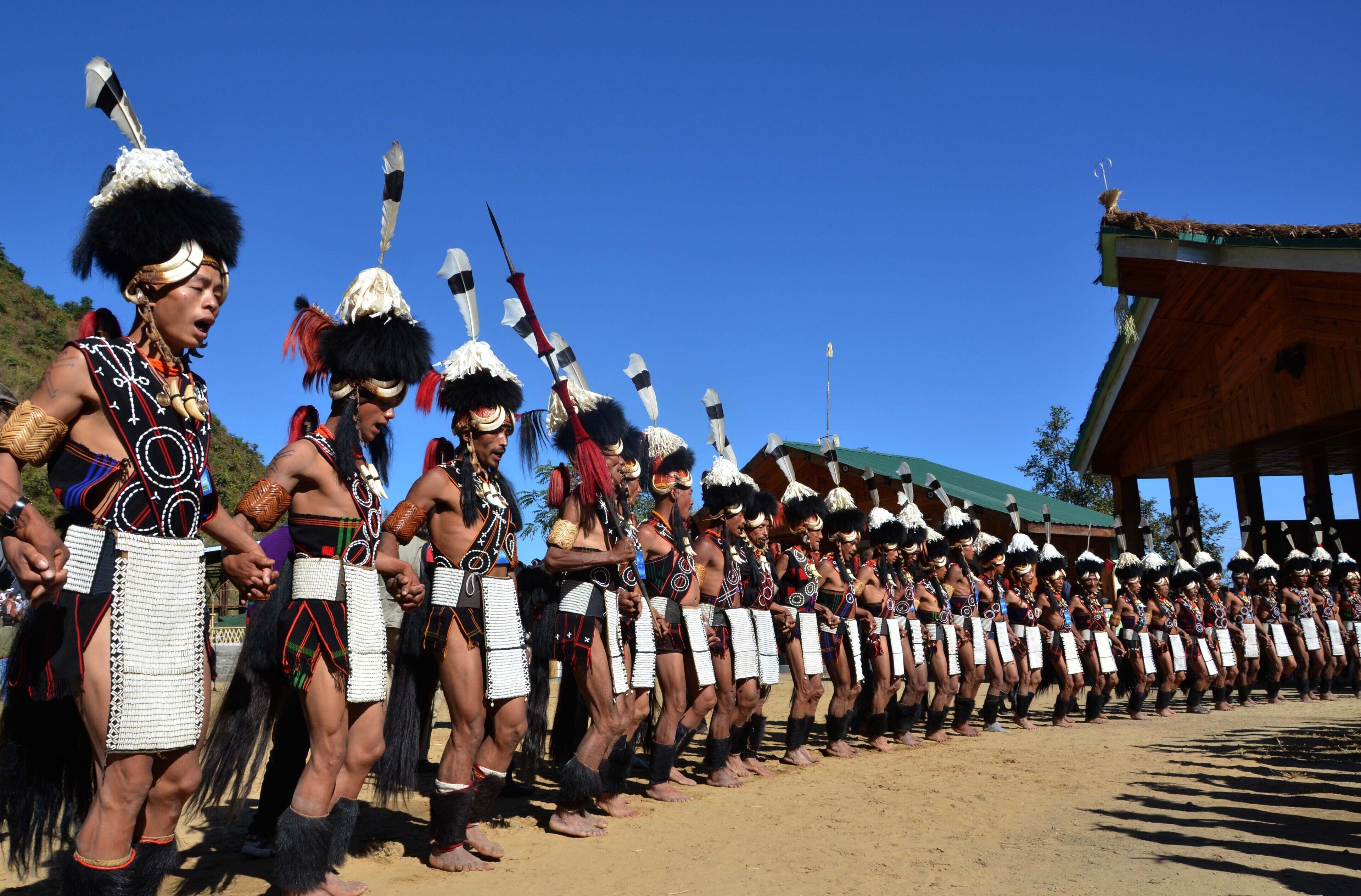 Um grupo de pessoas vestindo trajes tradicionais, em fila, ao ar livre.