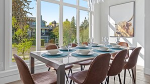 A dining area with a large window, a table set with blue placemats, and a framed picture on the wall. - Luxury Home in Quiet Neighborhood near Downtown with Fast Wi-F & 3 Workspaces (Calgary)