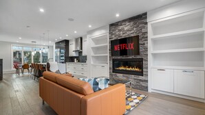 A modern living room with a leather sofa, a fireplace, and a Netflix sign on the wall. - Luxury Home in Quiet Neighborhood near Downtown with Fast Wi-F & 3 Workspaces (Calgary)