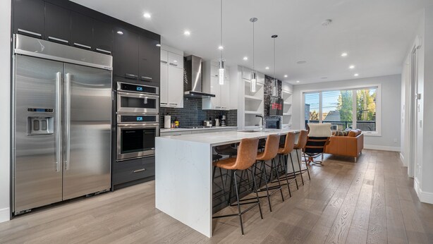 A modern kitchen with stainless steel appliances, a central island with bar stools, and a large window providing natural light. - Luxury Home in Quiet Neighborhood near Downtown with Fast Wi-F & 3 Workspaces (Calgary)