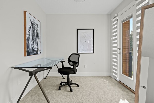 Un espace de bureau moderne avec un bureau en verre, un fauteuil de bureau noir et deux œuvres d’art encadrées accrochées au mur.