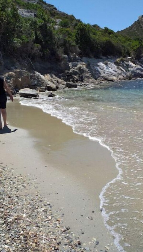 A beach with clear water, pebbles, and a rocky cliff in the background.