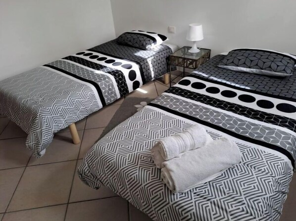 A room with two beds, each with patterned bedding and a small bedside table with a lamp. - Farm Stay (Moltifao)