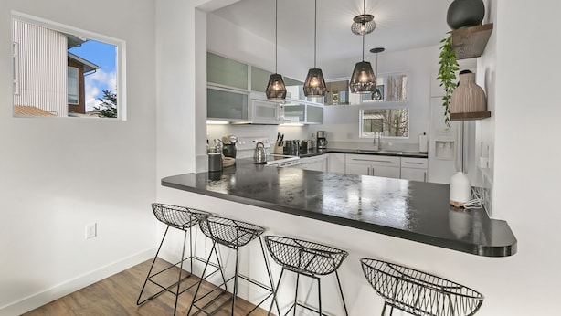 Une cuisine moderne dotée d’un grand îlot central, de tabourets de bar, de luminaires suspendus et offrant une vue sur l’extérieur.