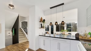 Une cuisine moderne avec des armoires blanches, un plan de travail en bois et des luminaires suspendus.