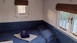 Ein kleines Zimmer mit Etagenbett, einem Fenster mit Vorhängen, einem Heizkörper und einem Stuhl.