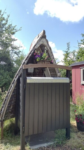 A small garden shed with a sloped roof and a flat door, situated in a grassy area surrounded by trees.