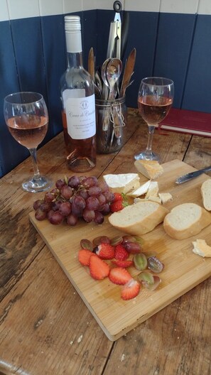 A wooden table with a bottle of wine, two glasses, a cheese board with grapes and strawberries, and a red book. - Stompy's hut - Cosy hut in very peaceful location (Laxfield)